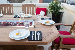 Rooftop fire dining table set with white plates and glasses along a burner of dark red fire stones