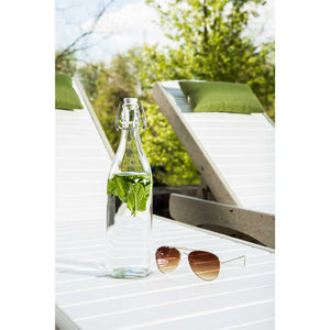 Glass water bottle with mint and aviator sunglasses resting on a white slatted poly sun lounger with a green pillow