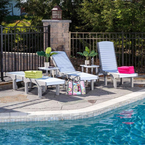 Gray and white poly sun loungers with reclined and upright backs, side tables and towels beside a pool and iron fence