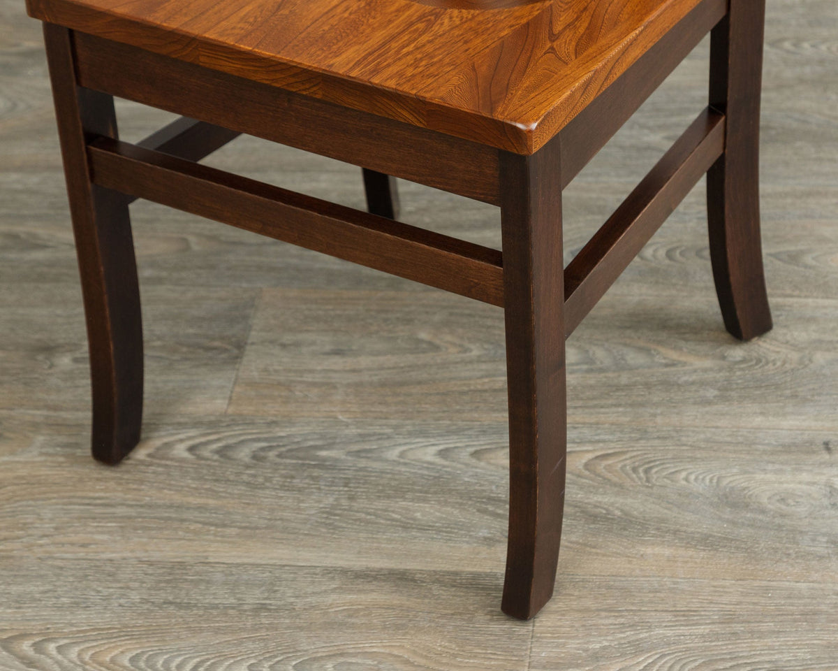 Detail of a dining chair base showing the cherry seat edge, dark stained legs and side stretchers on gray flooring