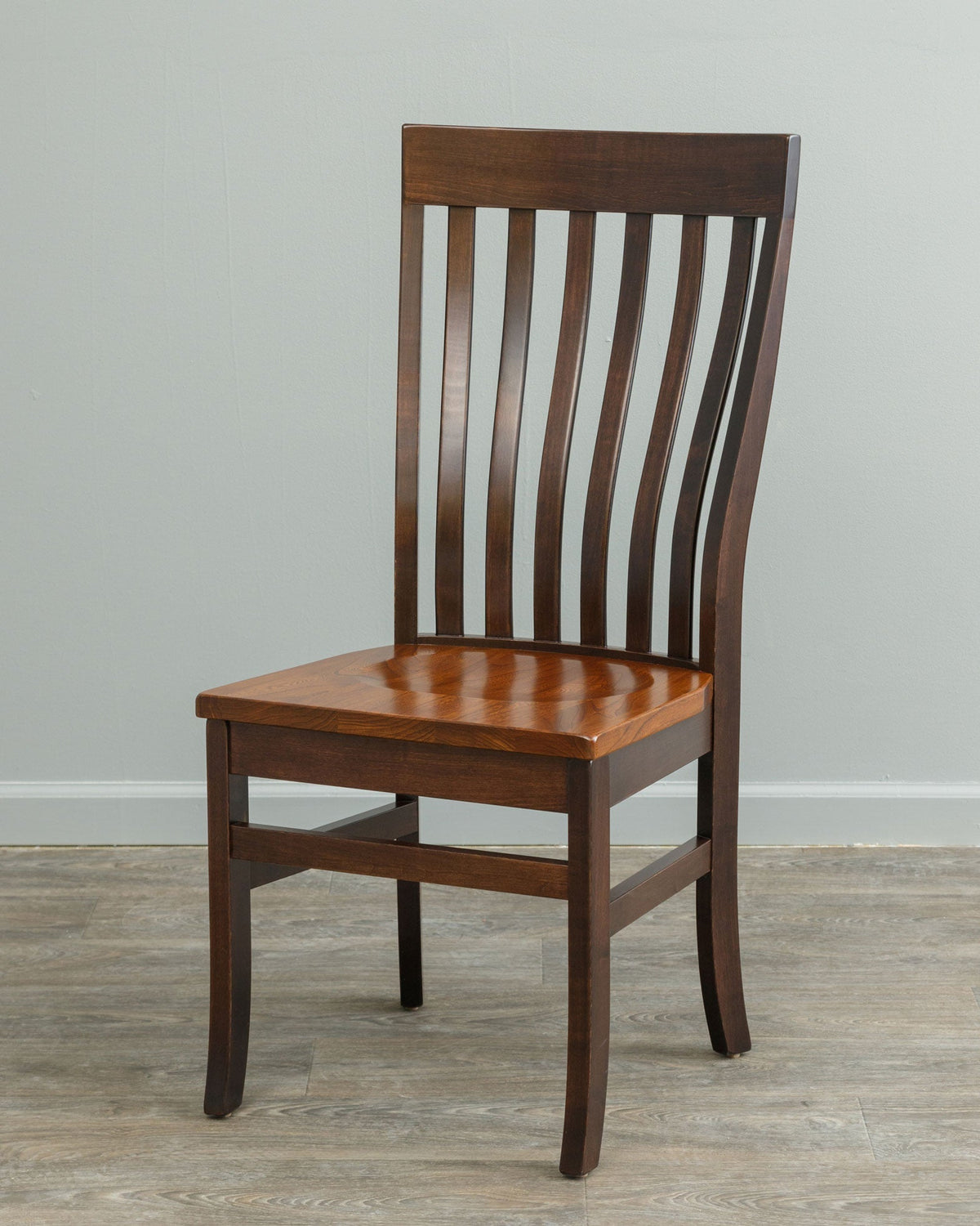 Lumbar dining chair with a dark brown frame, curved slat back and honey cherry seat, shown from an angle by a gray wall