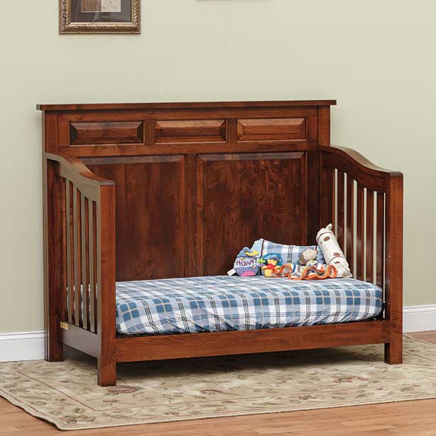 Cherry finish convertible crib converted to a day bed with slatted ends, raised panel headboard and plaid bedding in a nursery