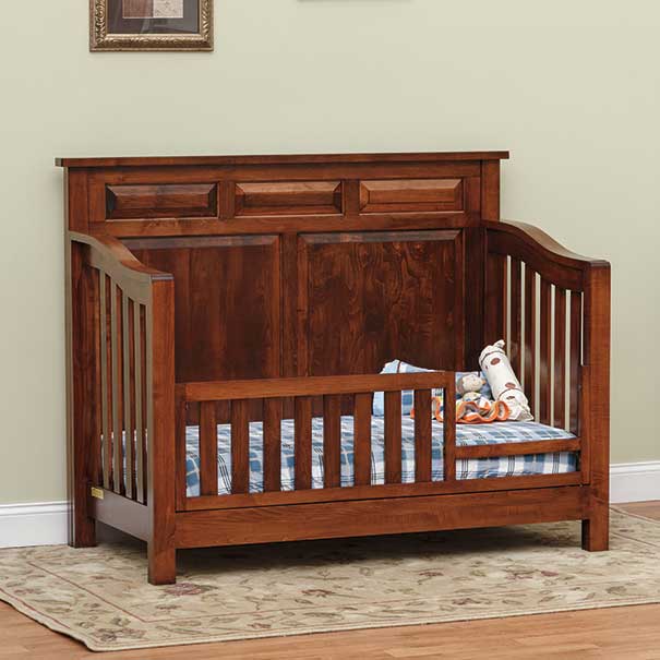 Toddler bed conversion of the Amish crib in warm cherry, with slatted safety rail across the open side and plaid mattress bedding
