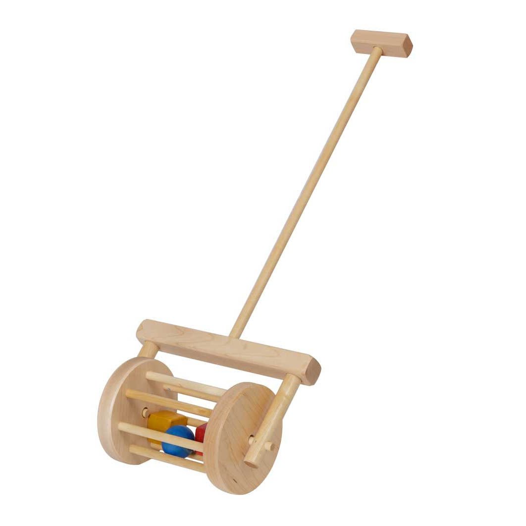 Blond toddler in a gray shirt pushing a wooden block roller push toy across a rug by a brick fireplace