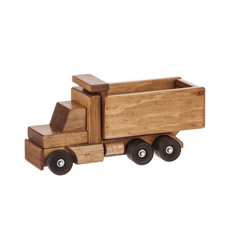 Boy in a white shirt kneeling on a rug tipping the bed of a wooden toy dump truck by a brick fireplace