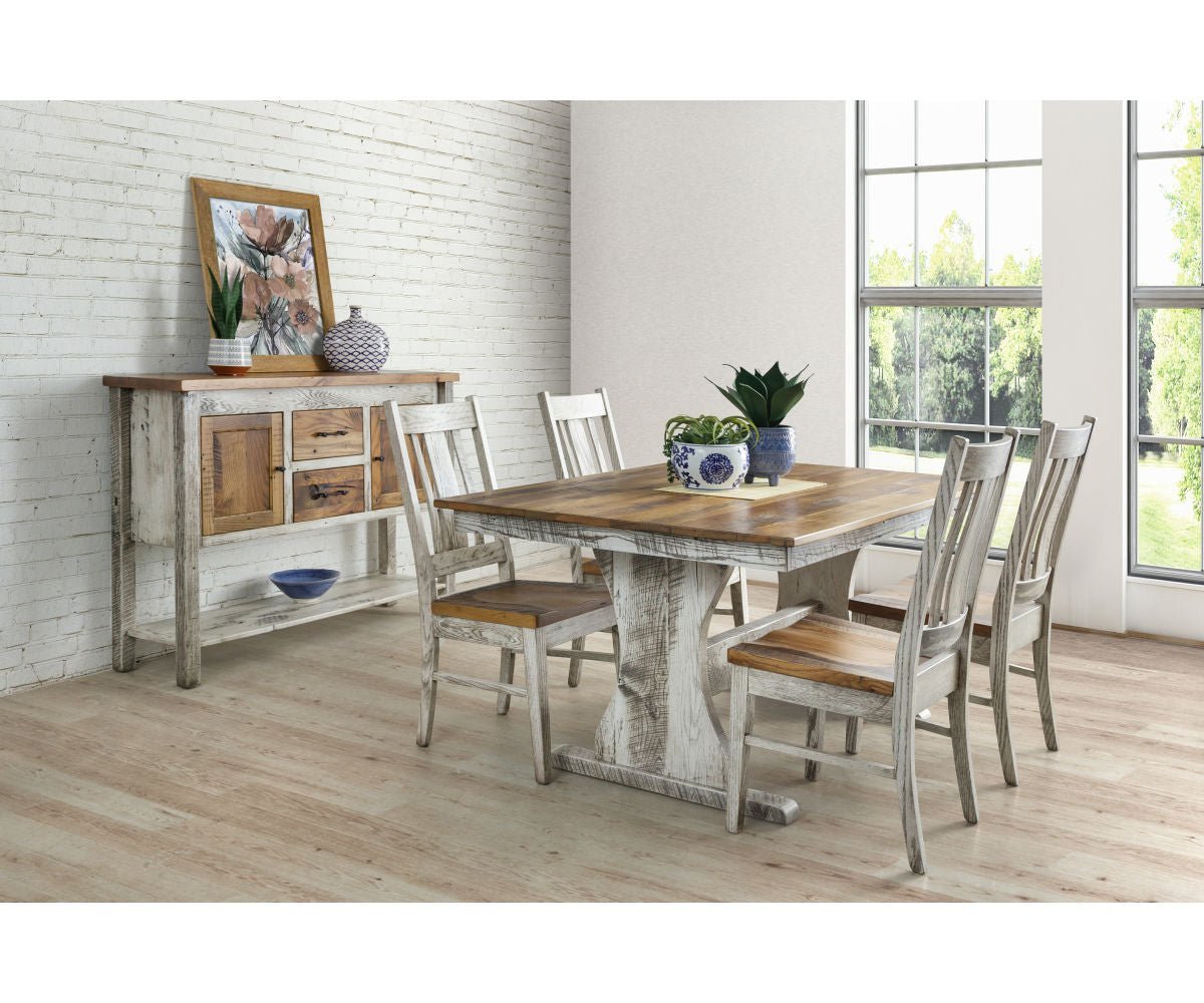 Whitewashed trestle table and four chairs beside a distressed sideboard with framed art in a sunny dining room