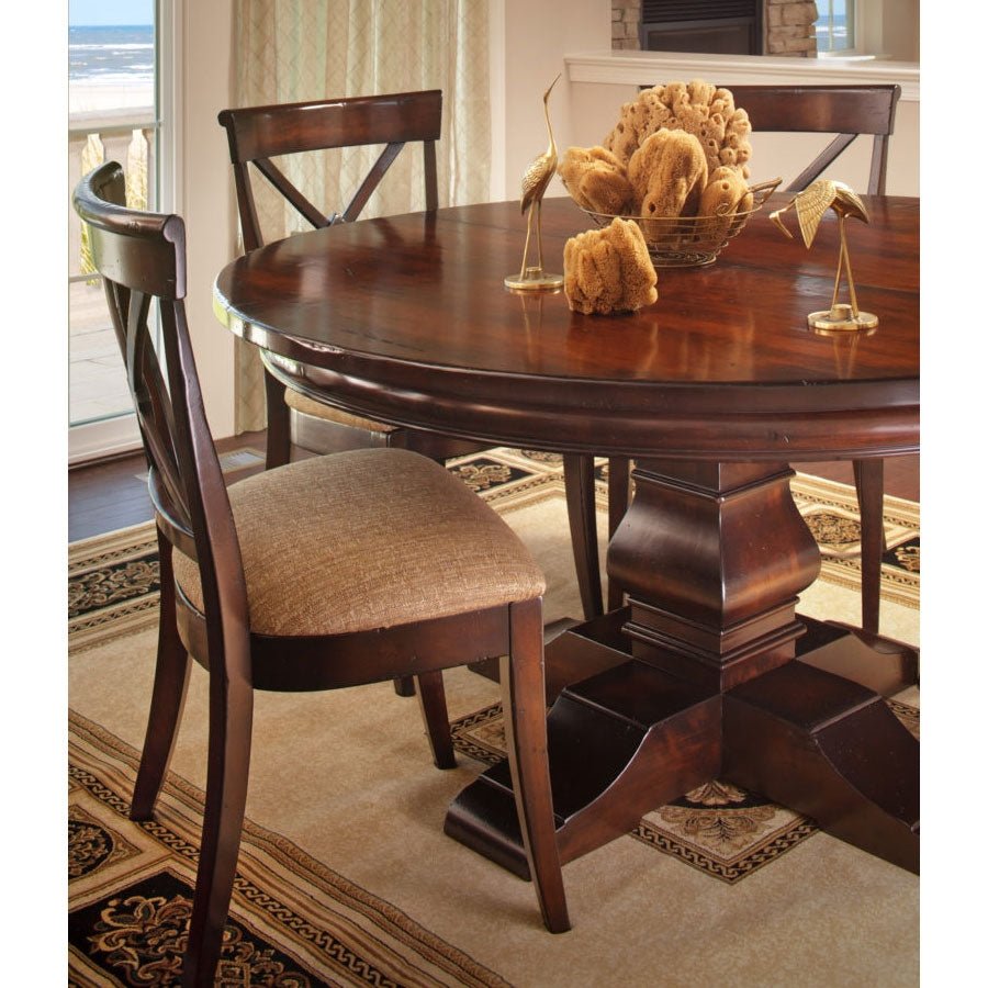 Round dark cherry pedestal dining table with a carved square pedestal and X-back chairs with tan cushioned seats