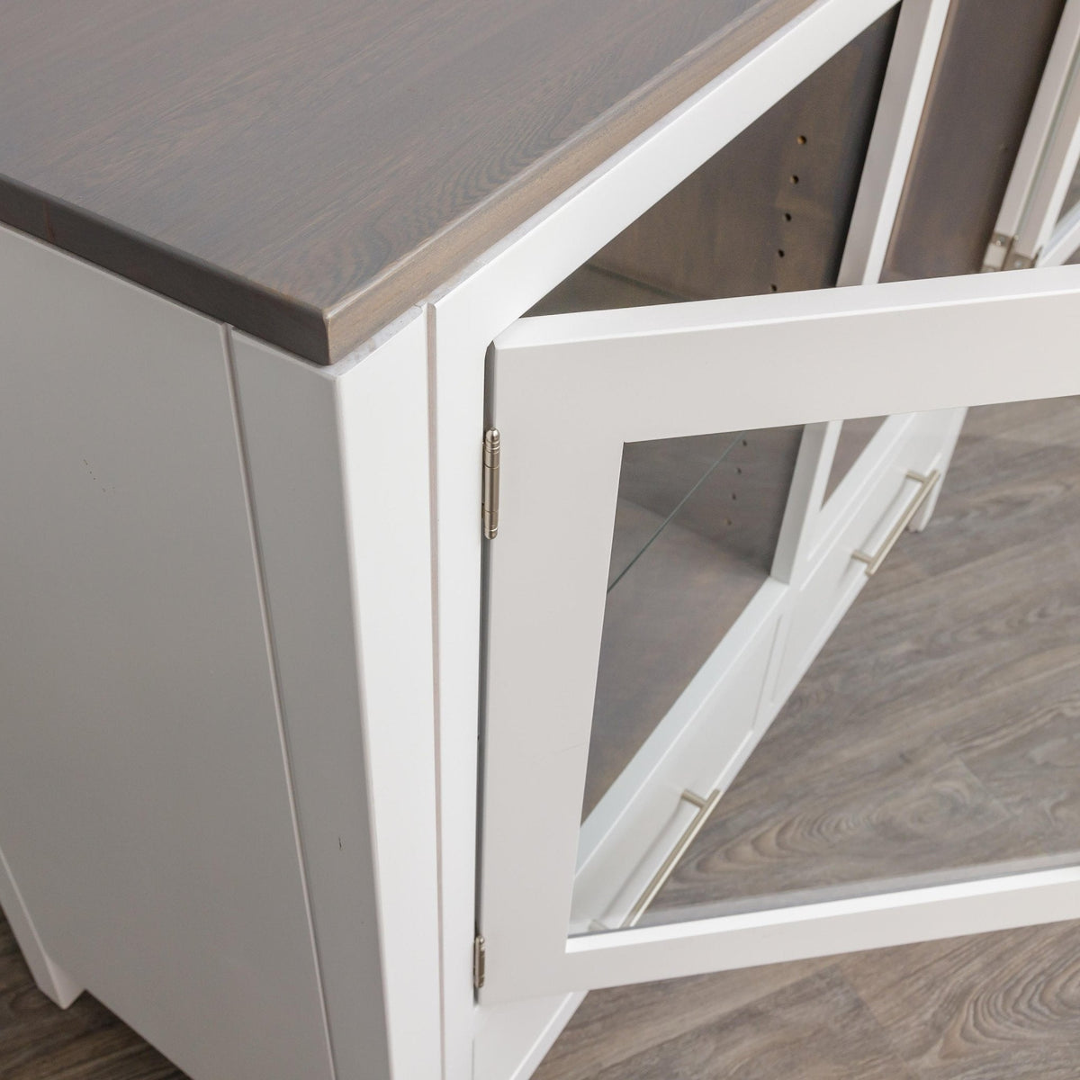 Corner detail of a white wine server showing the gray wood top, open glass door and nickel hinges