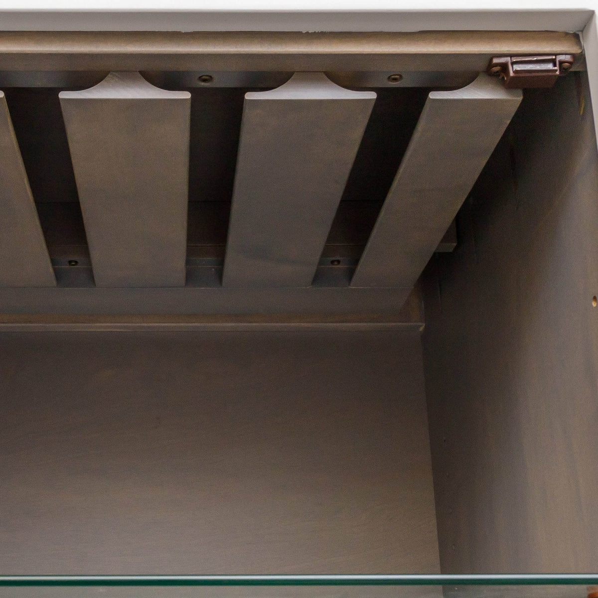 Close-up inside a wine cabinet showing the angled stemware glass holder rails above a glass shelf