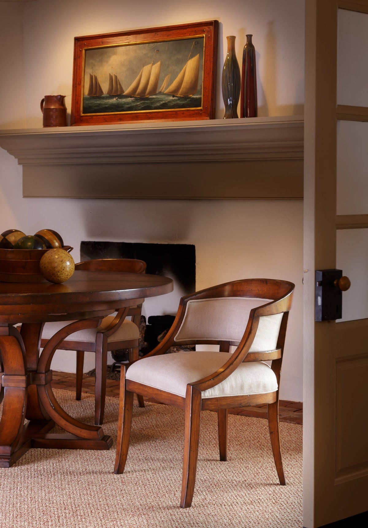 Upholstered cherry arm chair with a rounded frame and cream cushions at a round dining table in a warm room