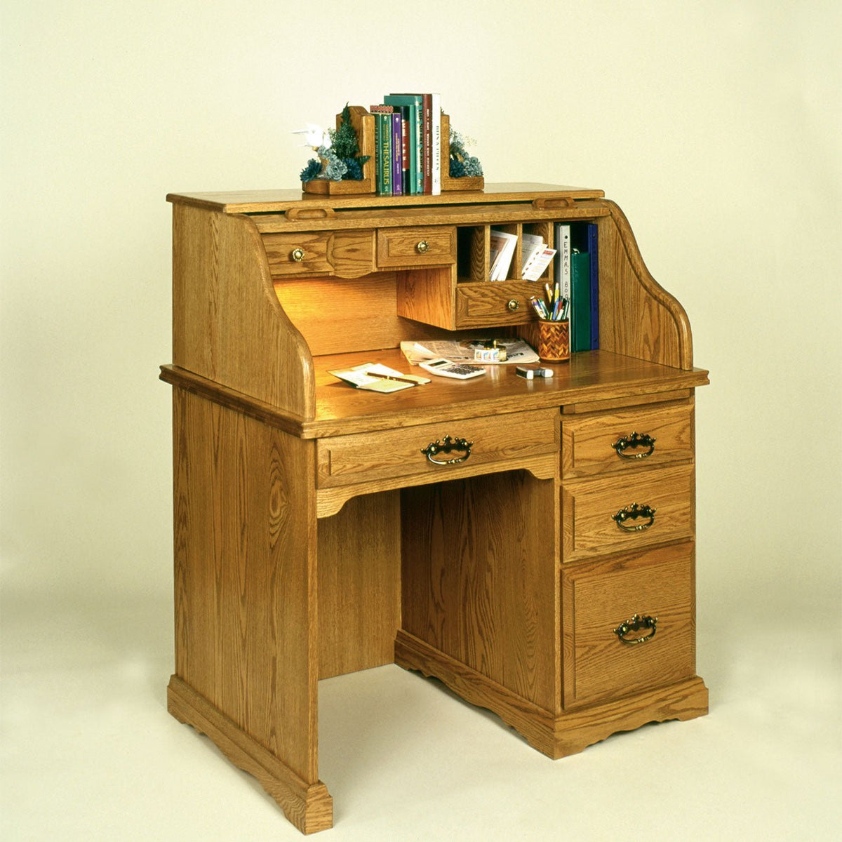 Single pedestal oak roll top desk with cubbies and small drawers open on a soft cream background