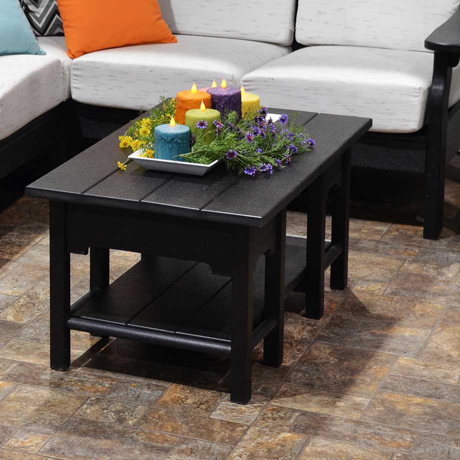 Black poly patio coffee table with a lower shelf and colorful candles on top, in front of a white cushioned sectional