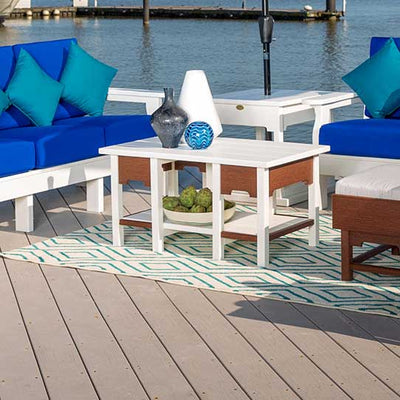 White and mahogany poly coffee table with a lower shelf on a dock, ringed by blue cushioned patio seating