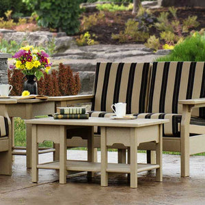 Tan poly coffee table with lower shelf holding books and mugs in front of black and cream striped patio chairs