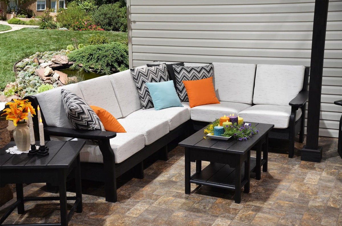 L shaped black poly patio sectional with white deep seating cushions, accent pillows and coffee table beside a pond