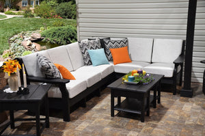 L shaped black poly patio sectional with white deep seating cushions, accent pillows and coffee table beside a pond