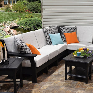 Black poly sectional sofa with white cushions and chevron pillows around a matching coffee table on a stone patio