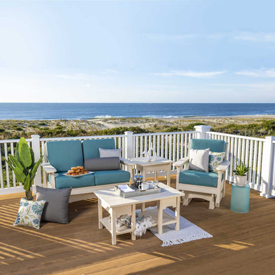 White poly glider loveseat, glider chair, side table and coffee table with teal cushions on a beachfront deck