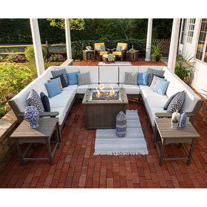 Evening patio with a U shaped sectional, white cushions, patterned pillows and a burning fire table on brick pavers
