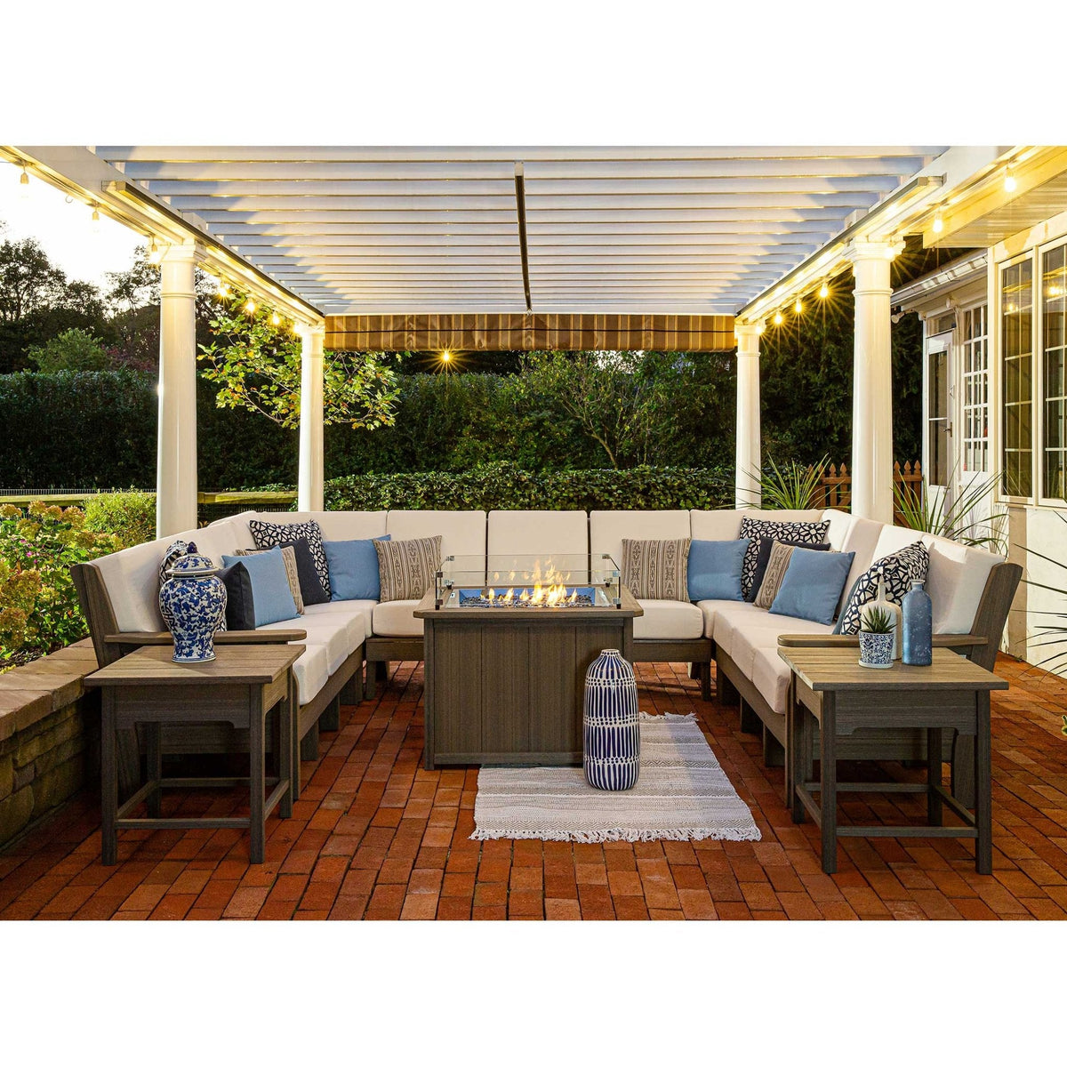 Gray poly sectional sofa set with cream cushions, blue and black pillows and end tables around a lit fire pit table