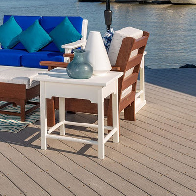 White poly patio side table with a plank top and stretcher base on a dock beside blue cushioned sectional seating