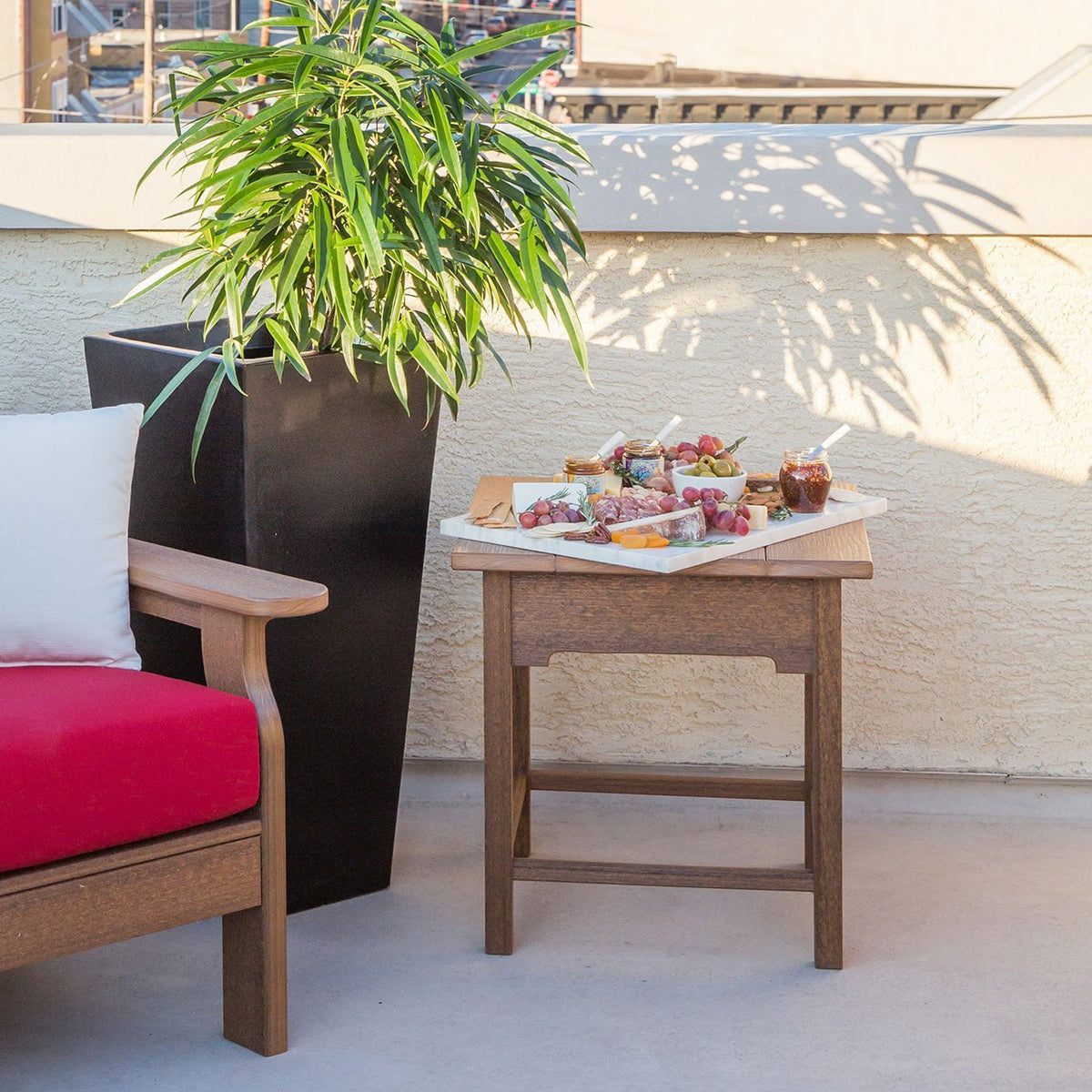 Antique mahogany poly side table holding a charcuterie board on a rooftop patio beside a red cushioned chair