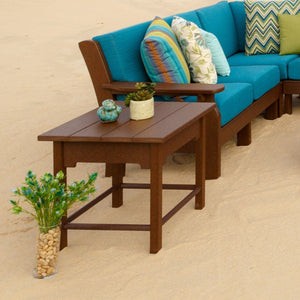 Brown poly patio side table with succulents on top, set in sand in front of a teal cushioned sectional sofa