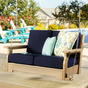 Porch swing with navy blue cushions, floral and mint accent pillows on a taupe poly frame beside a swimming pool