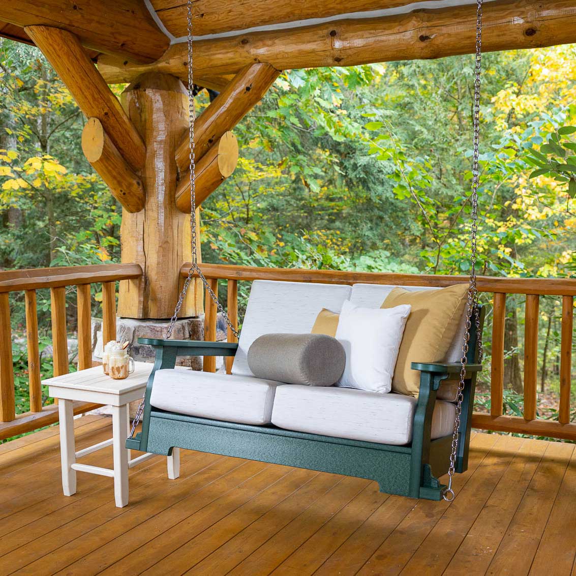 Deep-seating poly porch swing in turf green with light gray cushions and bolster pillow hanging by chains on a log cabin porch
