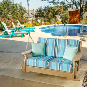Poly porch swing in weatherwood with blue striped Sunbrella cushions and aqua pillows hanging poolside on chains