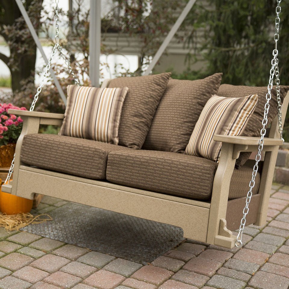 Angled view of the tan poly loveseat porch swing with chocolate brown Sundown cushions on a brick patio with mums