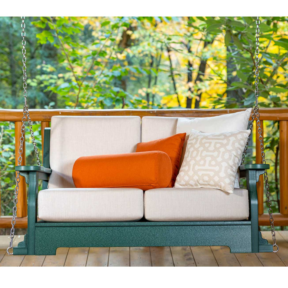 Green poly hanging porch swing with beige deep-seating cushions and orange bolster pillow on a wooded deck