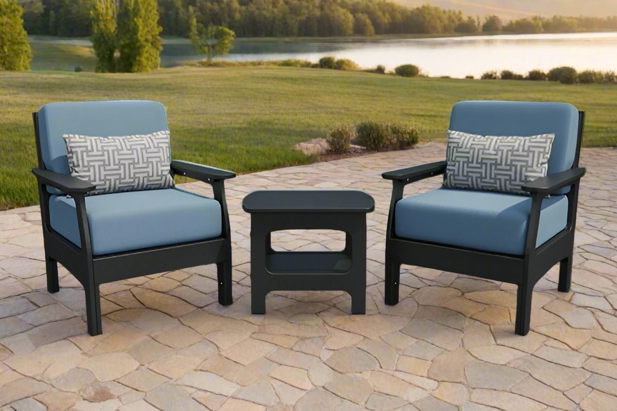 Two black poly patio club chairs with light blue cushions and patterned pillows flanking a small side table on a stone patio