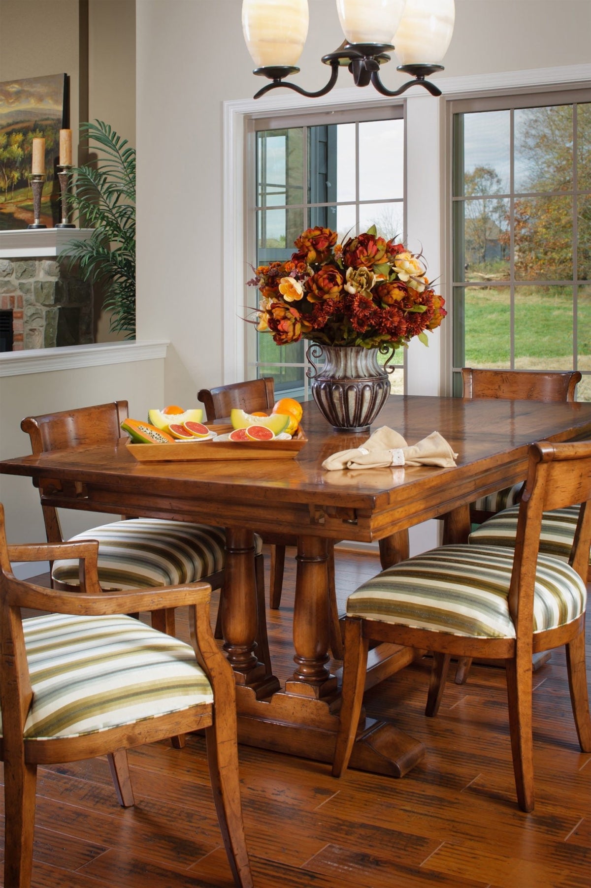 Rustic cherry trestle dining table with striped upholstered chairs, fruit tray and autumn floral centerpiece