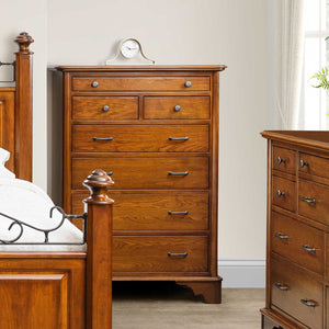Cherry chest of drawers with a clock on top, standing between an iron scroll bed and dresser