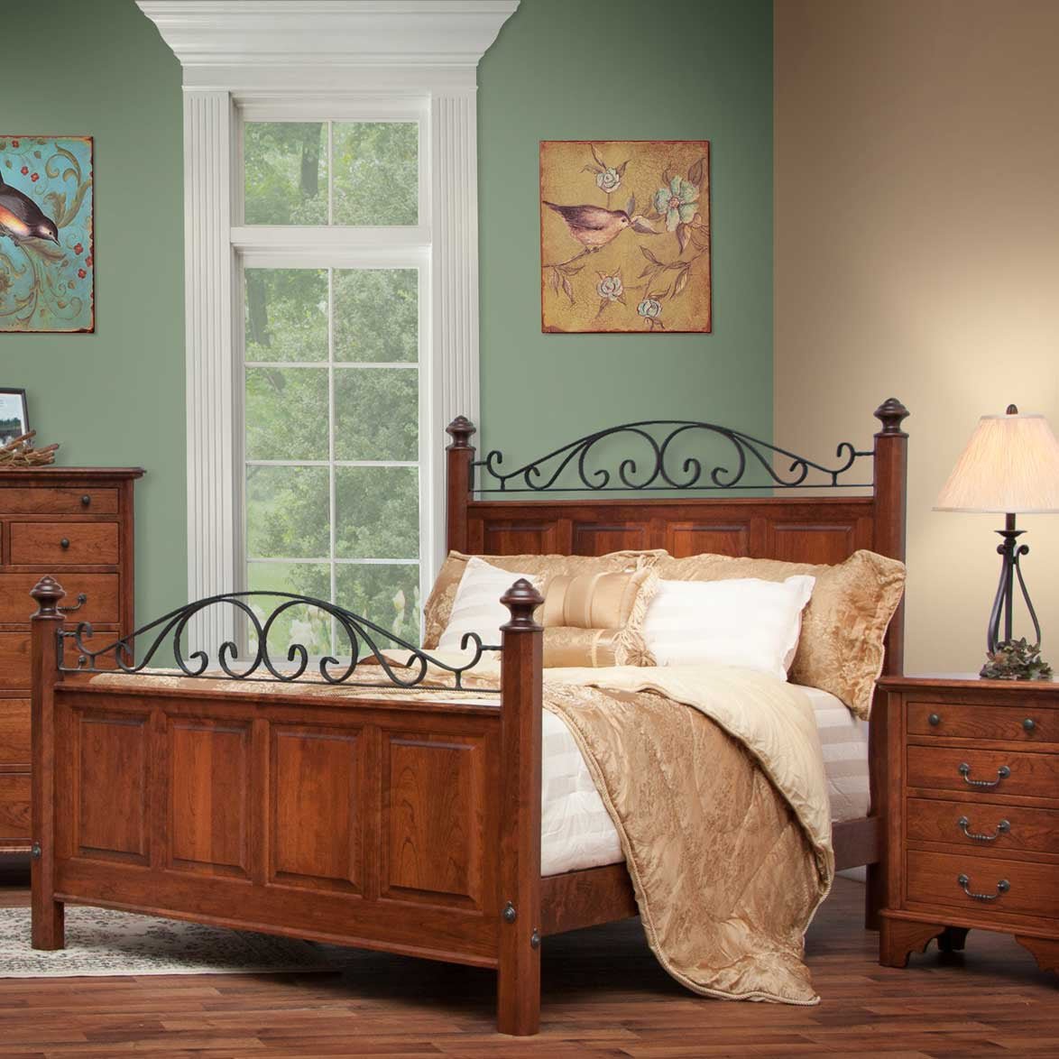 Iron scroll cherry bed with gold bedding in a green bedroom flanked by a chest and nightstand