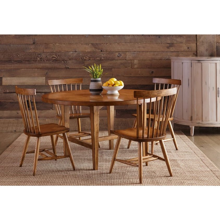 Round dining table set in golden maple with four spindle chairs, lemons and greenery in a rustic plank room