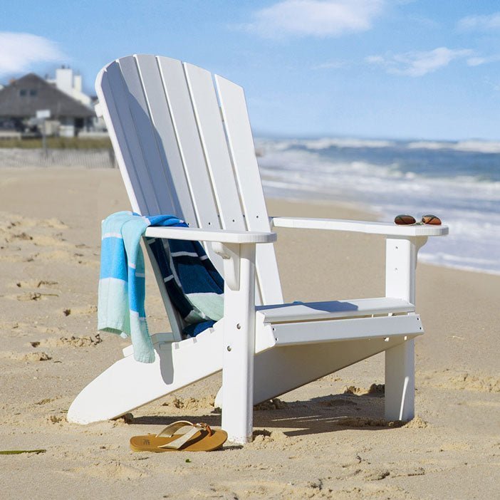 White poly fanback Adirondack chair on a sandy beach with a striped towel over the arm and flip flops in the sand