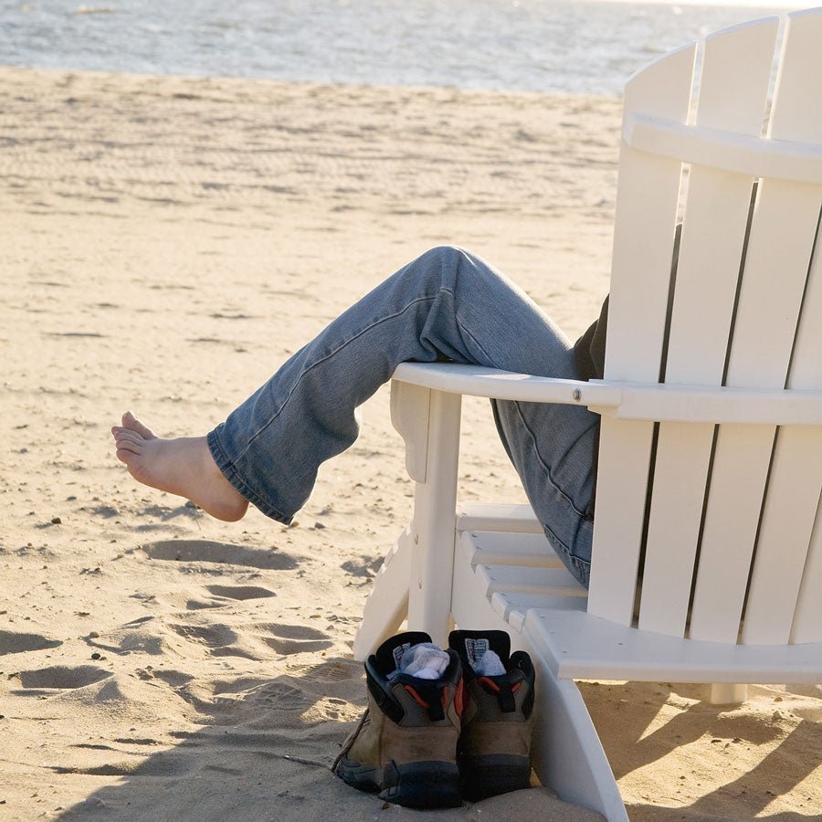 White poly fanback Adirondack chair on a sandy beach with a striped towel over the arm and flip flops in the sand