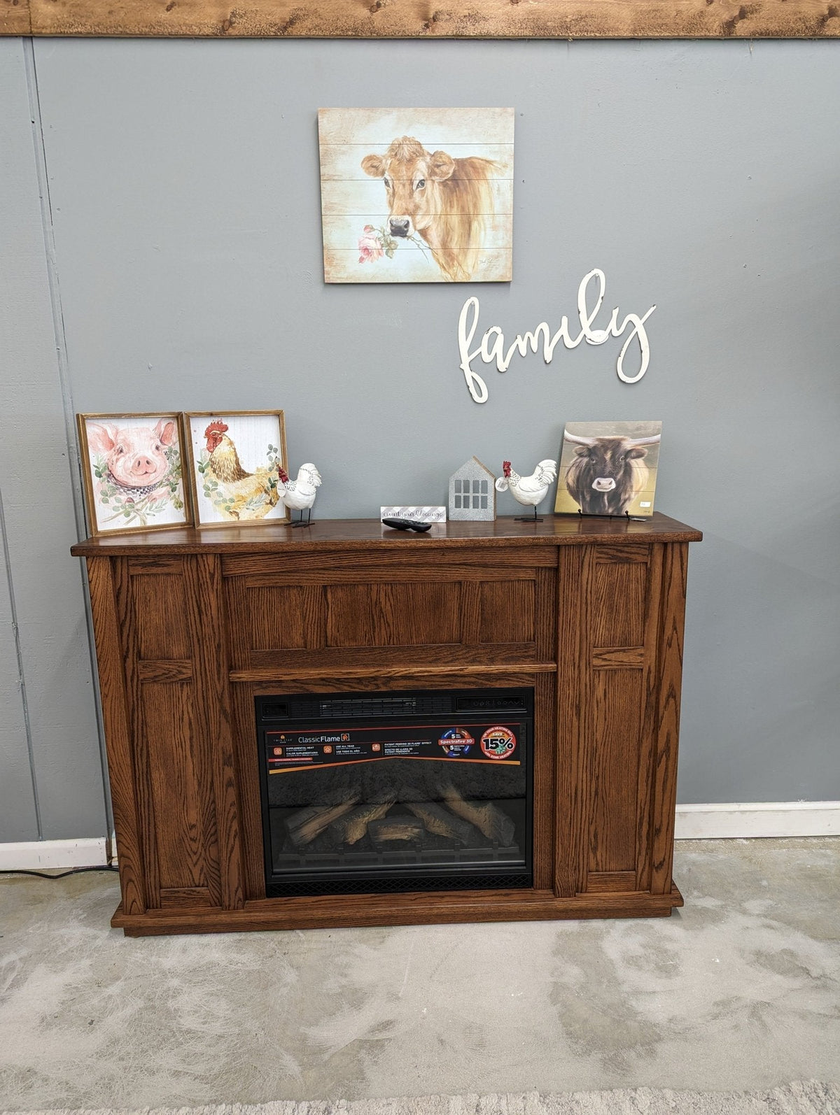 Oak electric fireplace mantel on a showroom floor decorated with farmhouse animal prints under a family sign