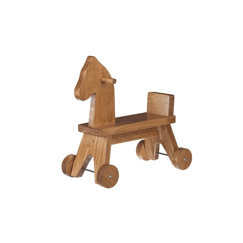 Toddler girl in pink straddling a natural wood ride-on horse with handle pegs and wheels on a living room rug
