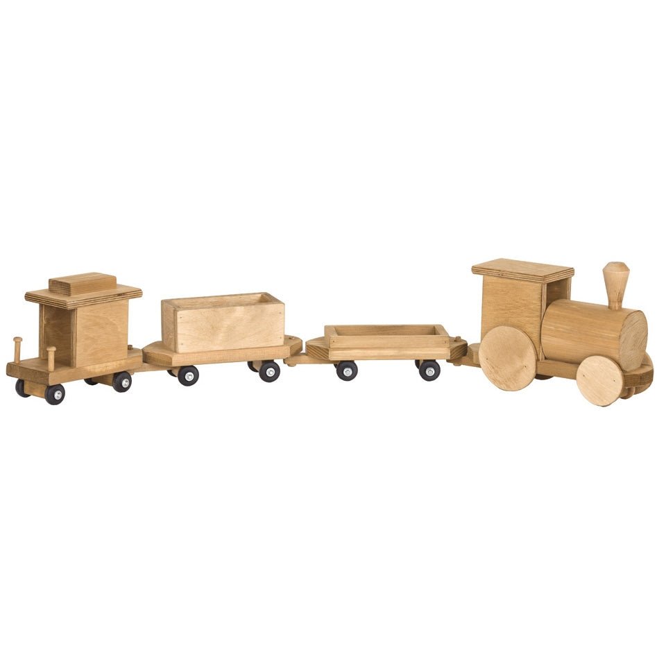Toddler in a pink romper pushing a wooden toy train with engine and cargo cars across a living room rug