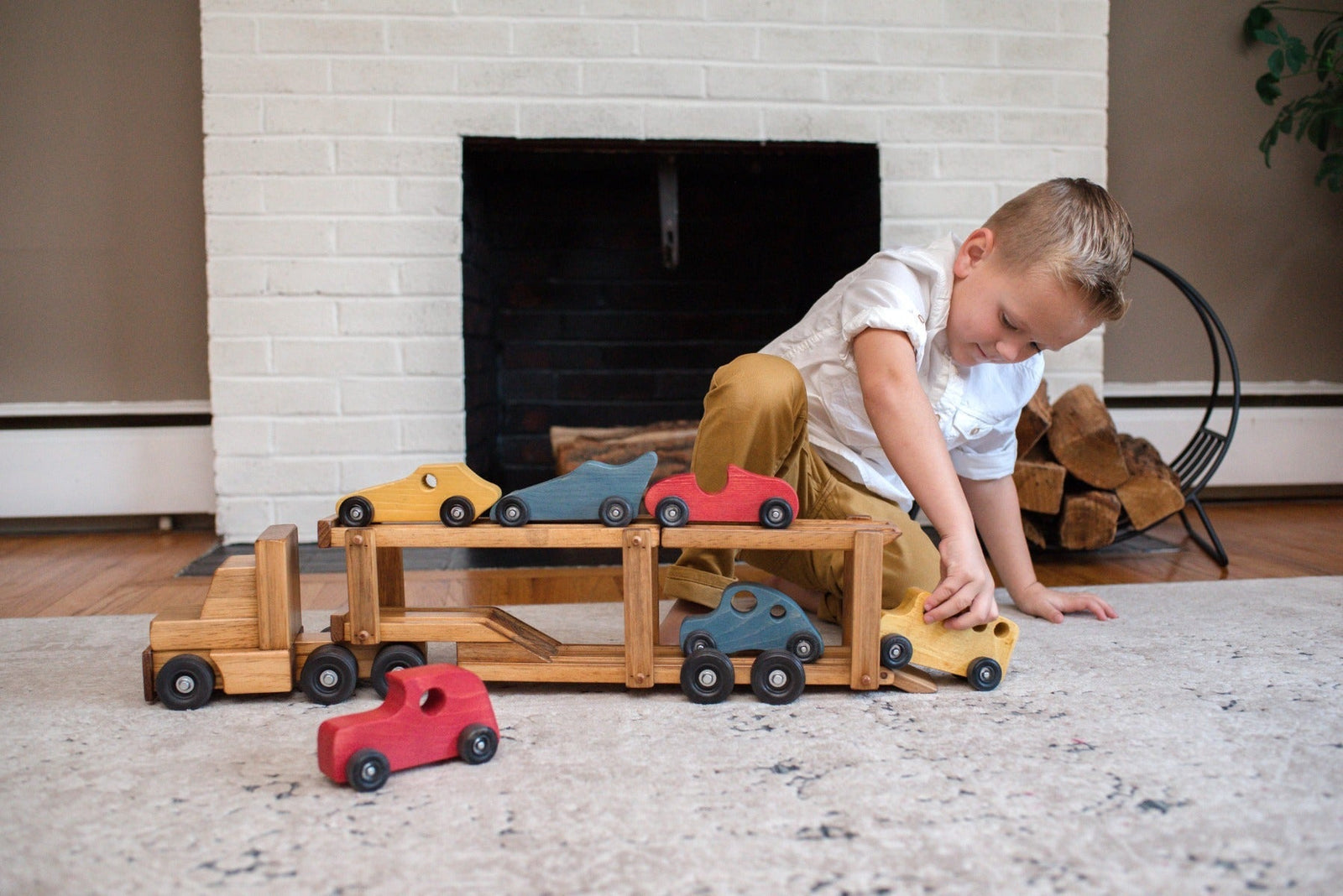 Boy loading small wooden cars onto a two-level wooden car carrier truck toy on a living room rug
