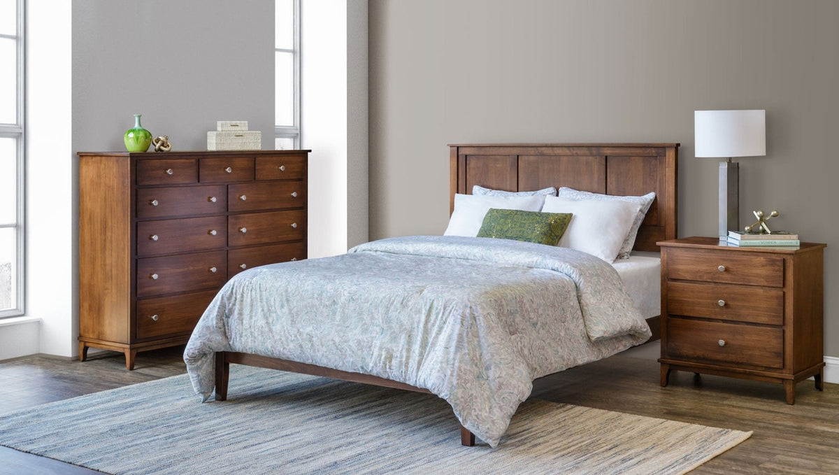 Modern Shaker bedroom set in warm medium brown wood with a panel bed, tall chest of drawers and three-drawer nightstand in a gray bedroom