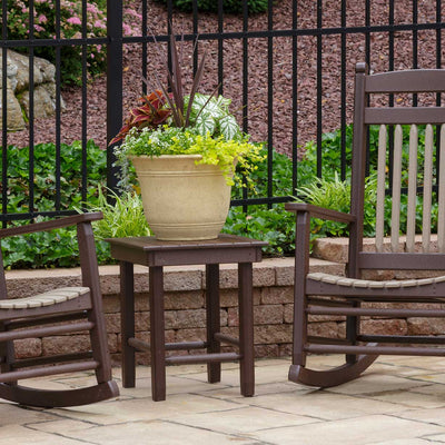 Two brown poly porch rockers with tan slat seats flanking a small square side table on a paver patio