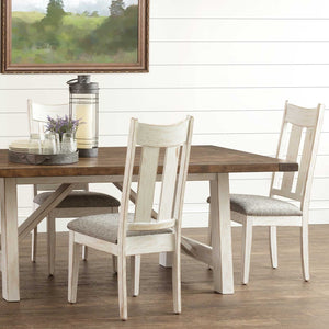 Whitewashed dining chairs with gray fabric seats around a trestle table with a natural brown plank top