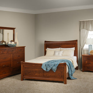 Cherry finished sleigh bed with a curved paneled headboard and matching footboard, dresser and nightstand in a warm bedroom