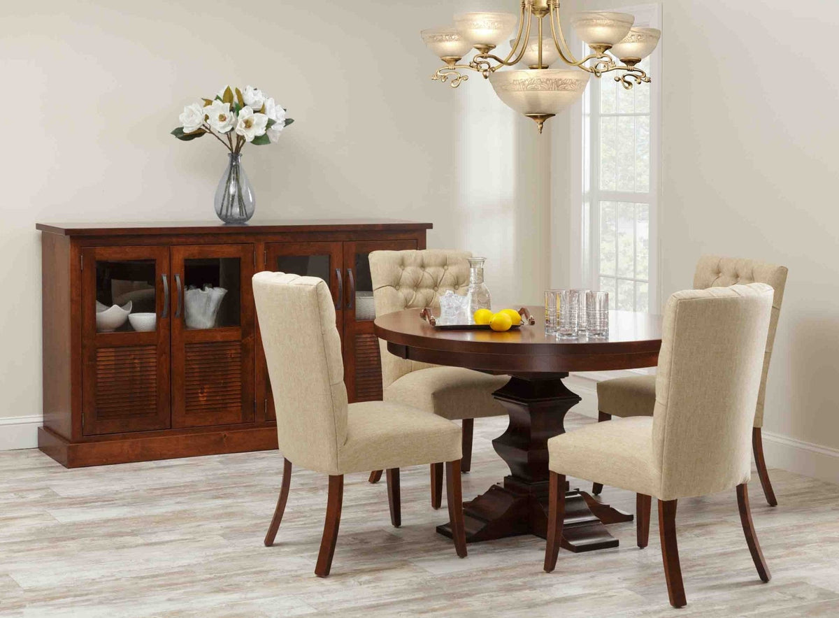 Cherry dining room with a four-door glass and louvered sideboard beside a round pedestal table and tufted upholstered chairs