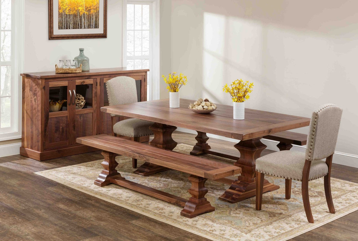 Rustic walnut trestle dining table with plank top and bench, paired with nailhead upholstered chairs and a louvered sideboard