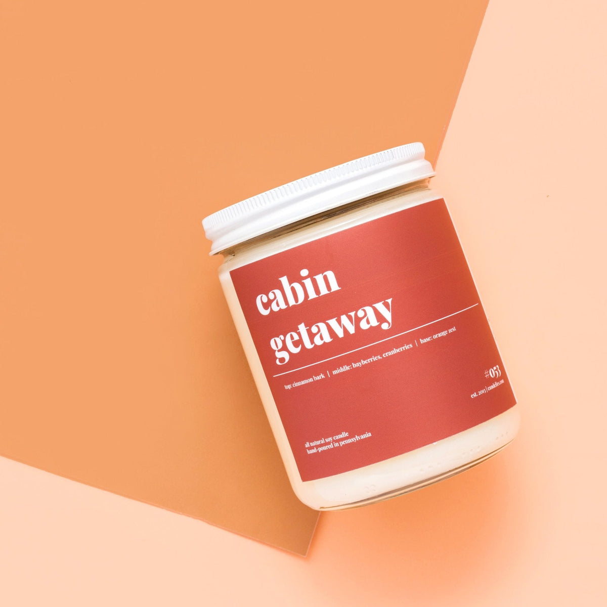 Standard cabin getaway soy candle photographed from above on a two-tone orange and peach paper background